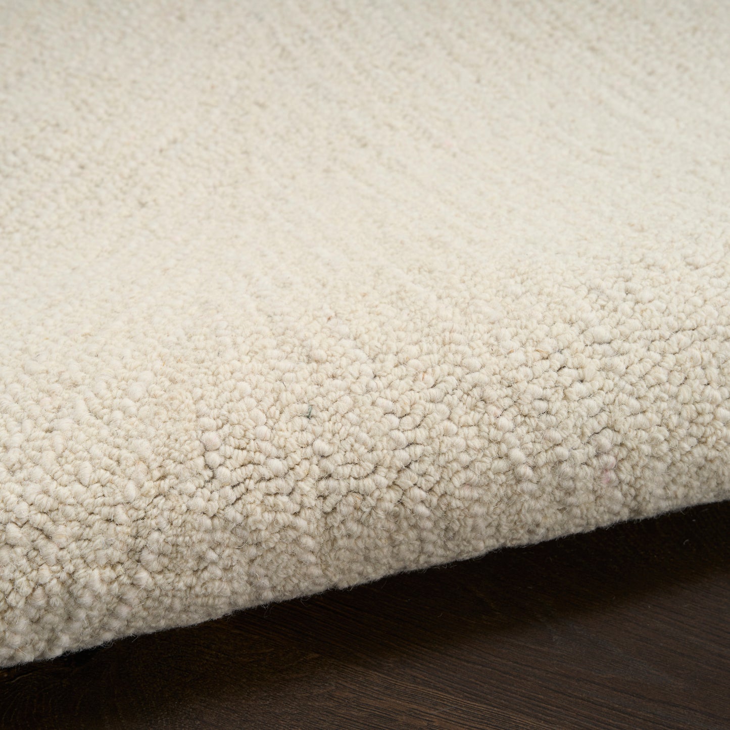 Cream textured loop-pile rug with dense plush loops, edge folded over on dark wood floor.