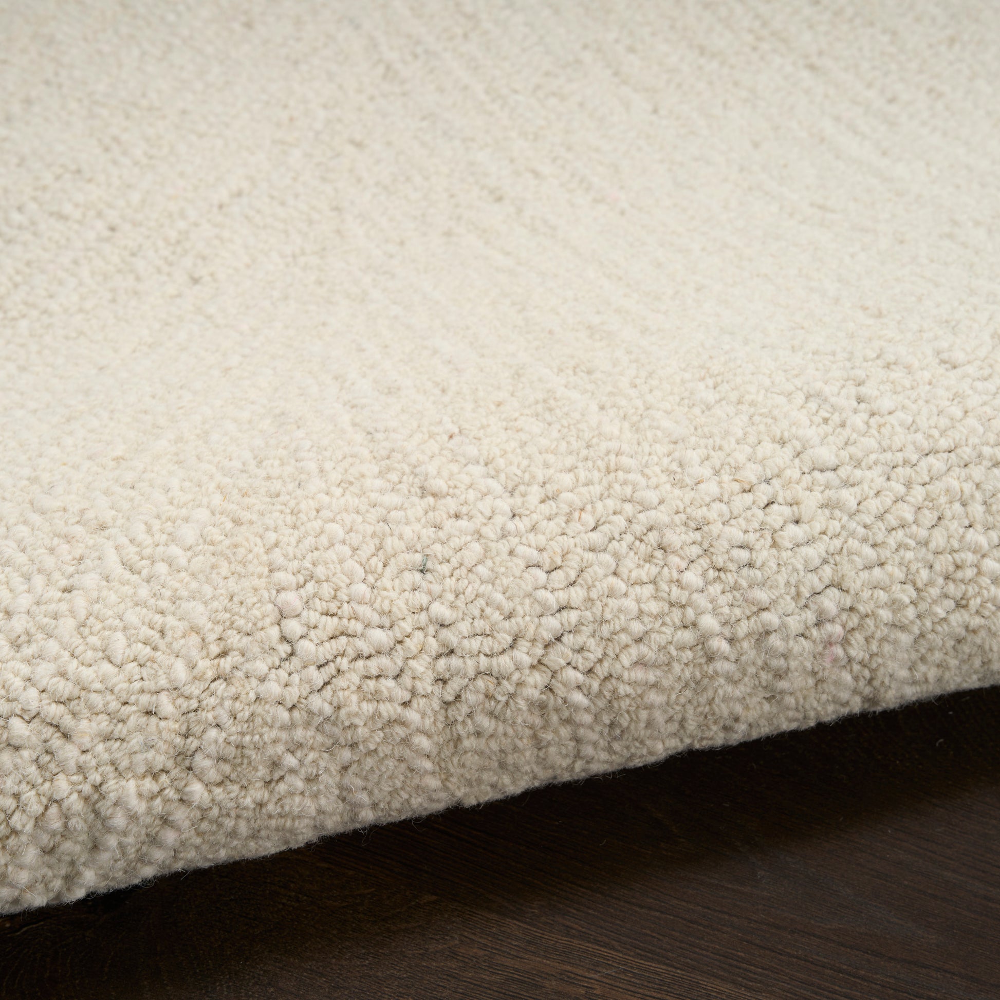 Cream textured loop-pile rug with dense plush loops, edge folded over on dark wood floor.
