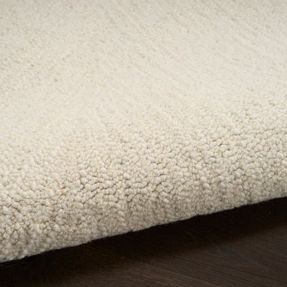Cream textured loop-pile rug with dense plush loops, edge folded over on dark wood floor.