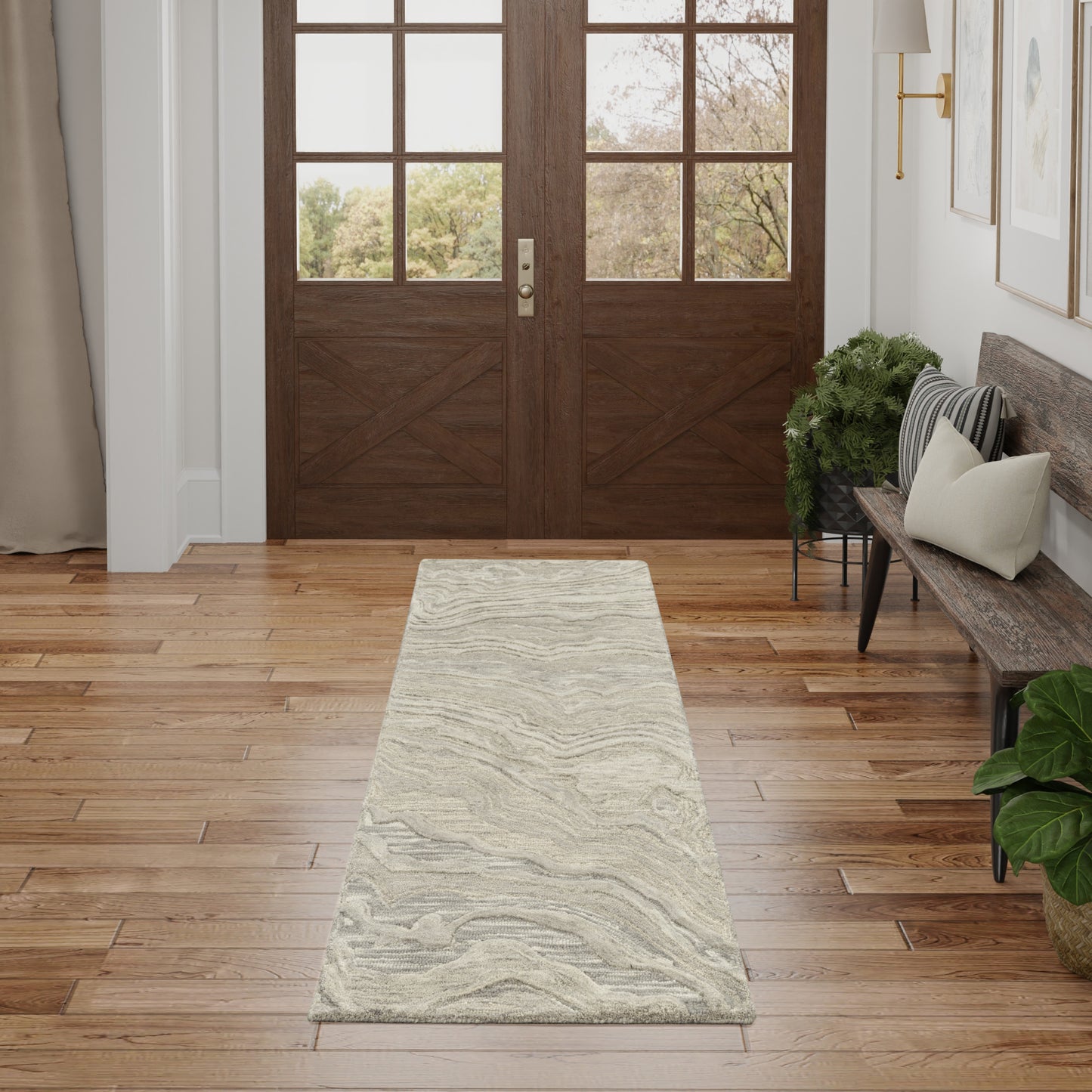 Long light-gray patterned runner rug on hardwood entry floor; wood-framed glass doors ahead, bench with cushions nearby.