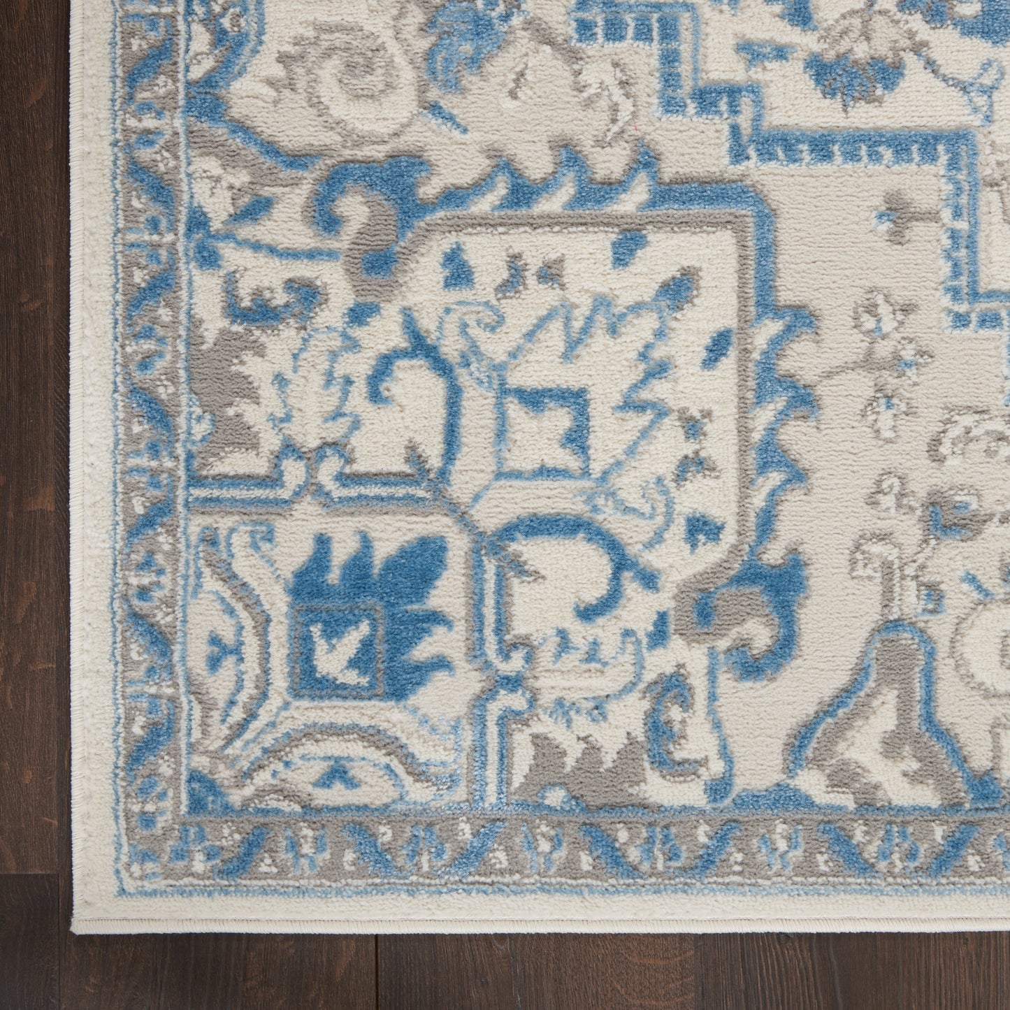 Close-up of ivory oriental rug corner with blue and gray floral motifs and a decorative border on dark wood floor.