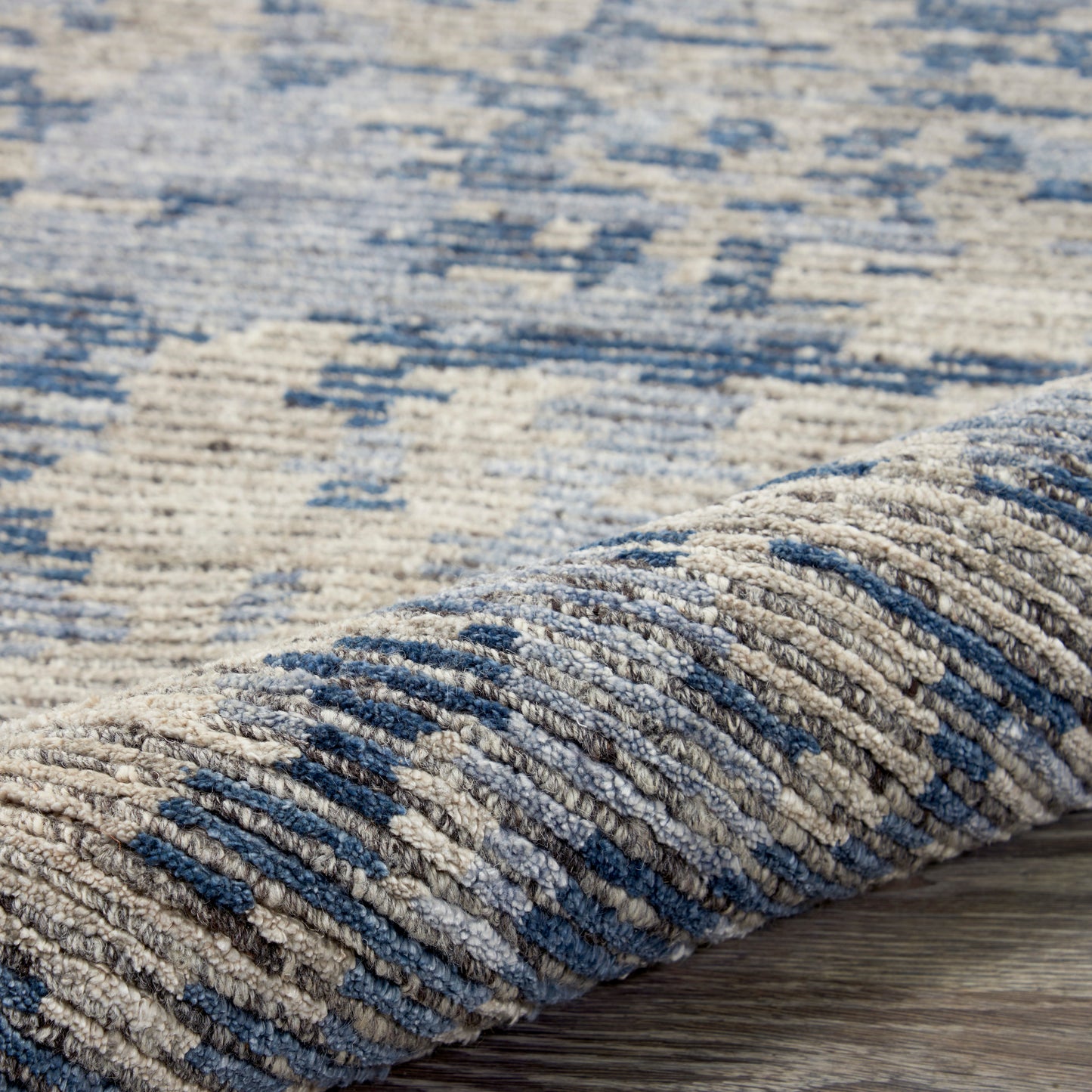 Blue and beige geometric patterned rug with thick pile; folded edge on a wooden floor.