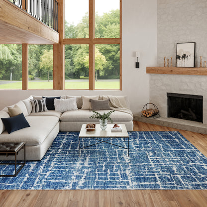 Bright living room with large windows, beige sectional, blue patterned rug, white coffee table, stone fireplace.