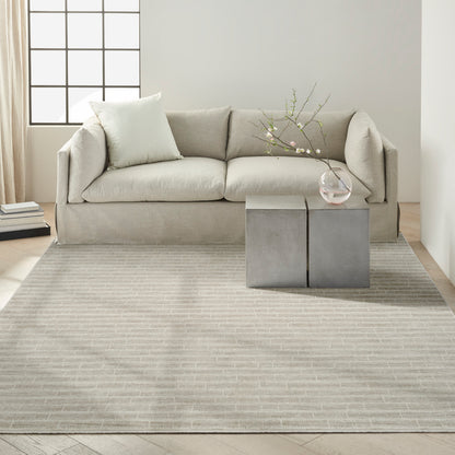 Beige modern sofa with pale cushions, concrete block coffee tables, glass vase with blossoming branch on striped rug.
