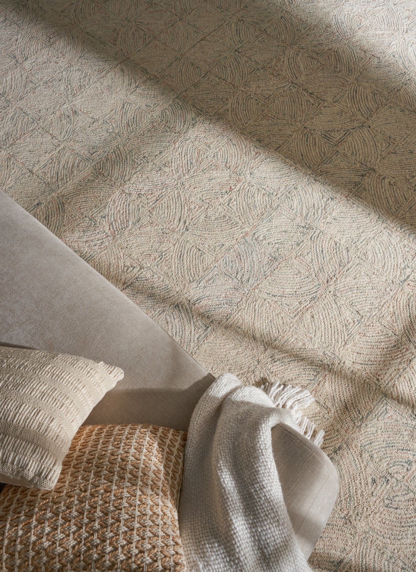 Neutral living room setup with grey sofa, cream textured pillow, tan woven pillow, and beige throw on a patterned rug.