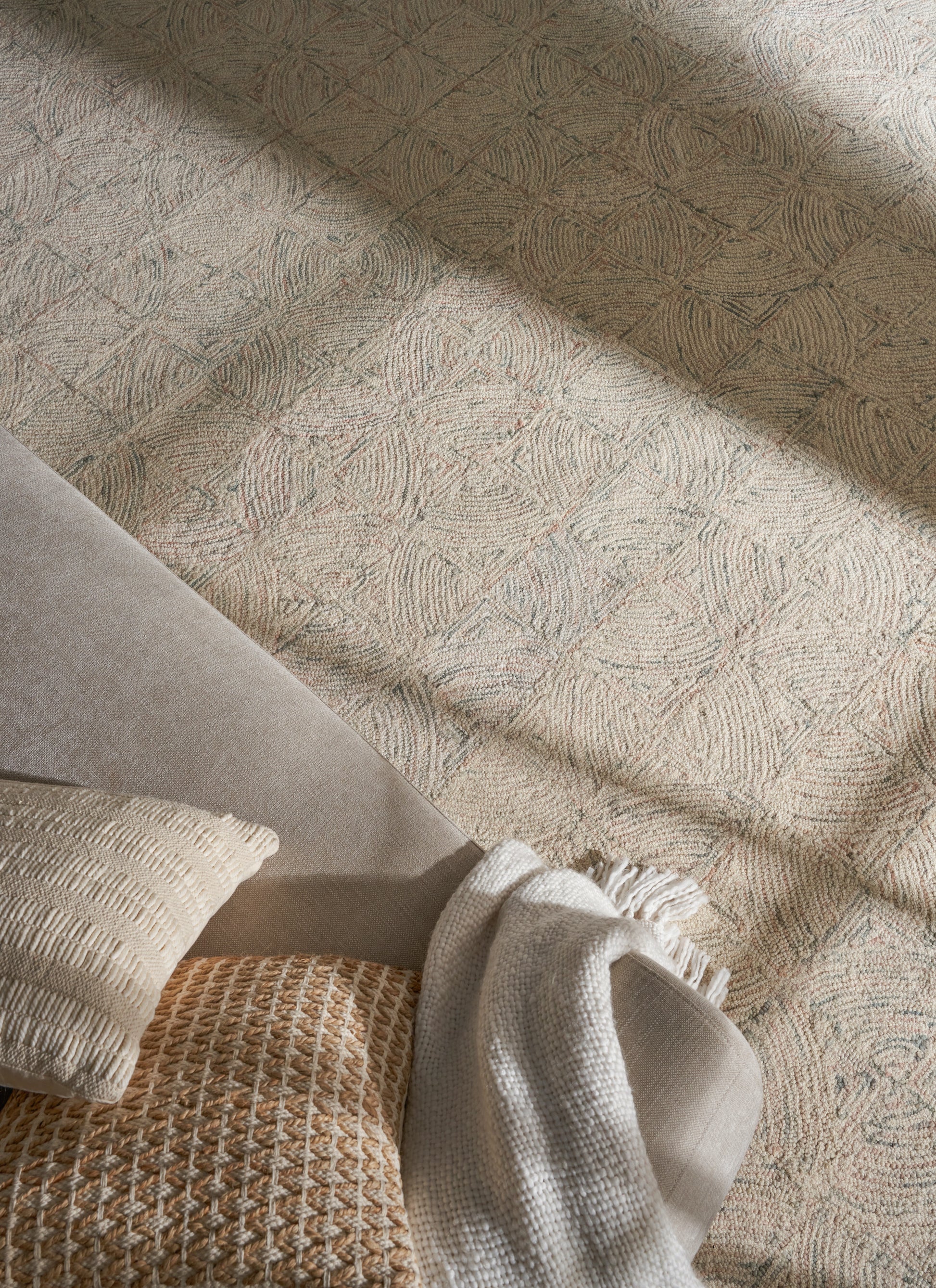Neutral living room setup with grey sofa, cream textured pillow, tan woven pillow, and beige throw on a patterned rug.