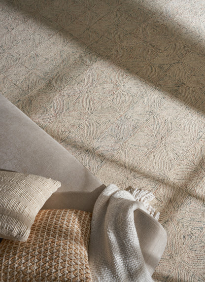 Neutral living room setup with grey sofa, cream textured pillow, tan woven pillow, and beige throw on a patterned rug.