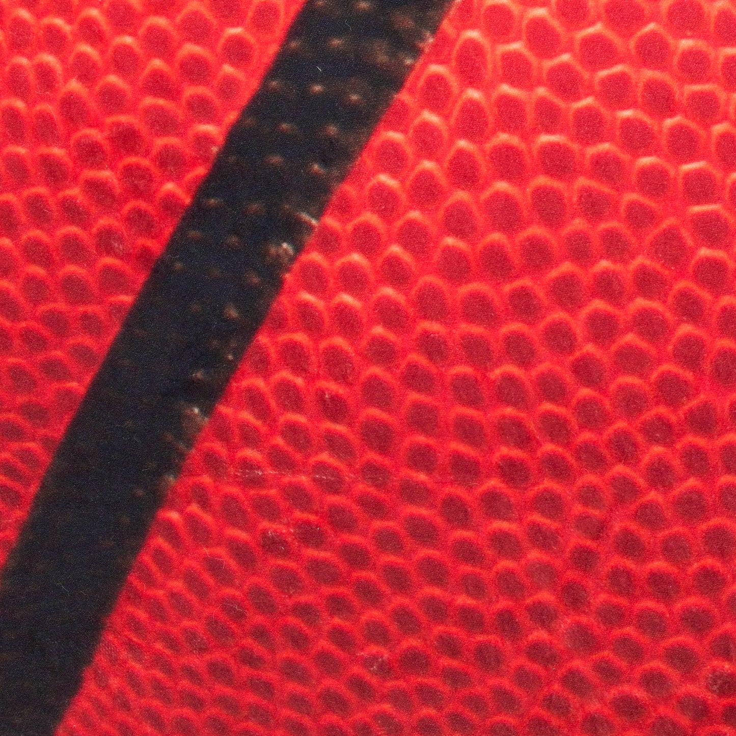 Macro shot of red pebble-grain basketball with bold black seam.
