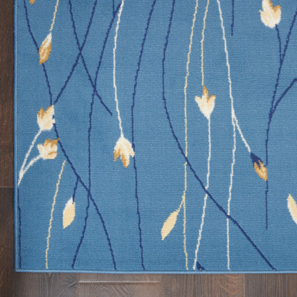 Blue area rug with flowing navy and white lines and small tan leaf motifs, laid on dark wooden floor.