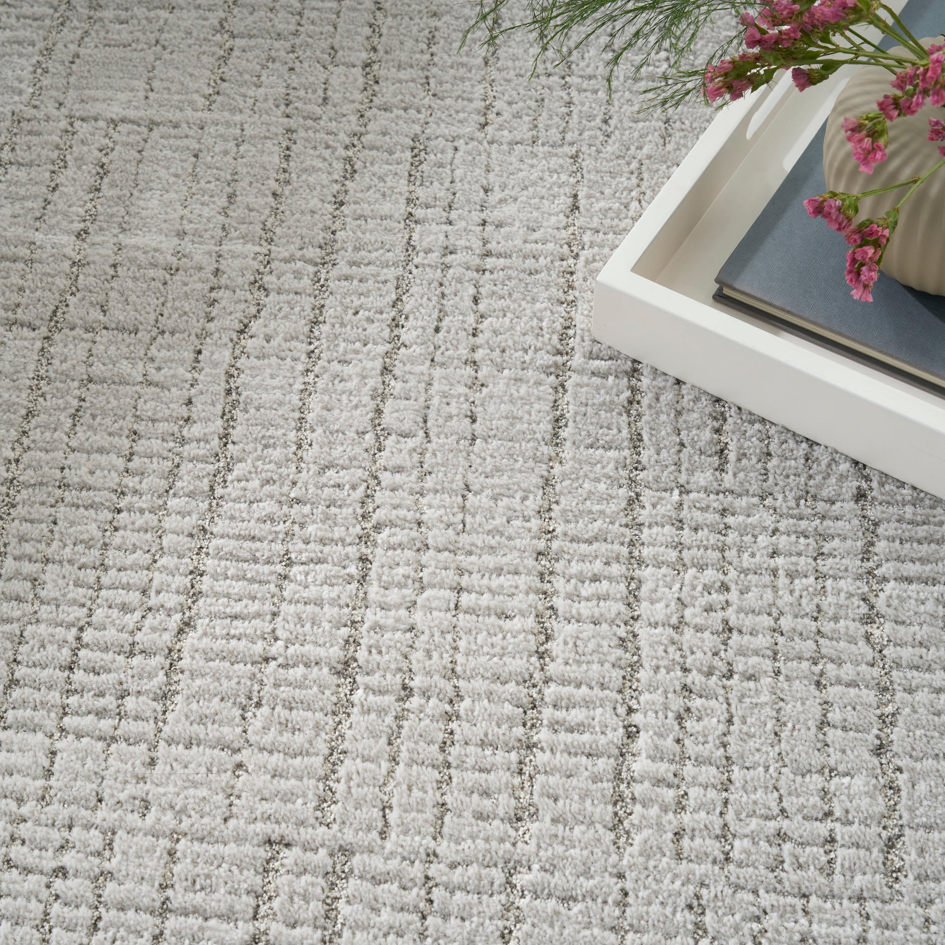 Light gray patterned rug with a white rectangular tray holding a blue-gray book and pink flowers.