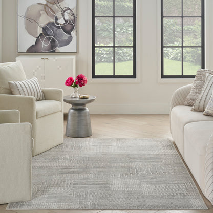 Neutral gray patterned area rug in a light beige living room with cream sofas, a metallic side table & pink flowers.