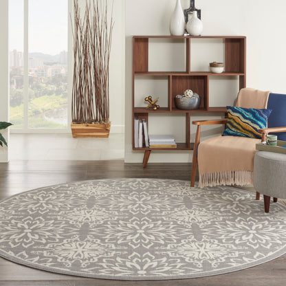 Round gray patterned rug in a modern living room with a wood bookshelf, beige throw, and twig planter.