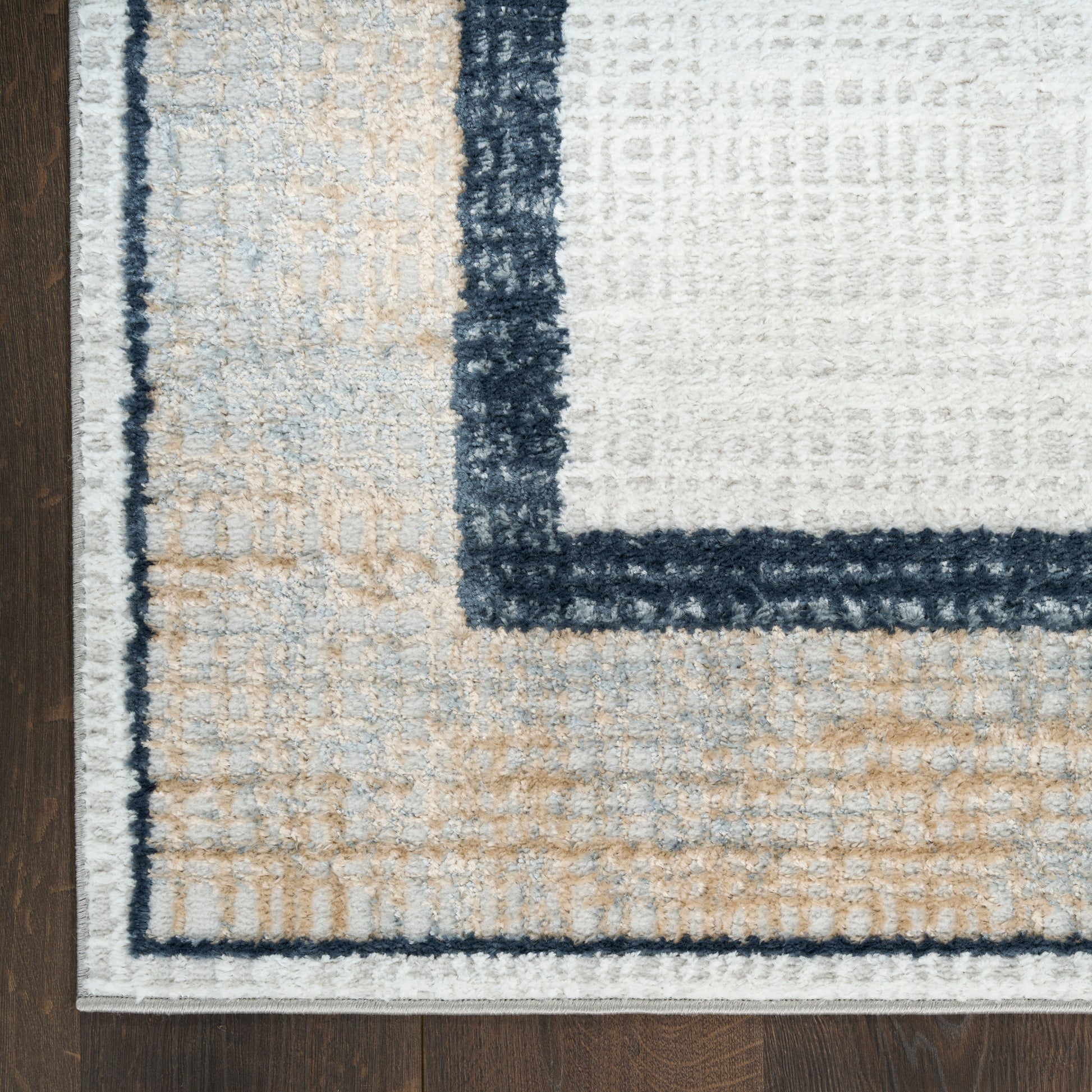 Close-up of a plush beige, white and navy geometric area rug with a dark blue border on a wood floor.