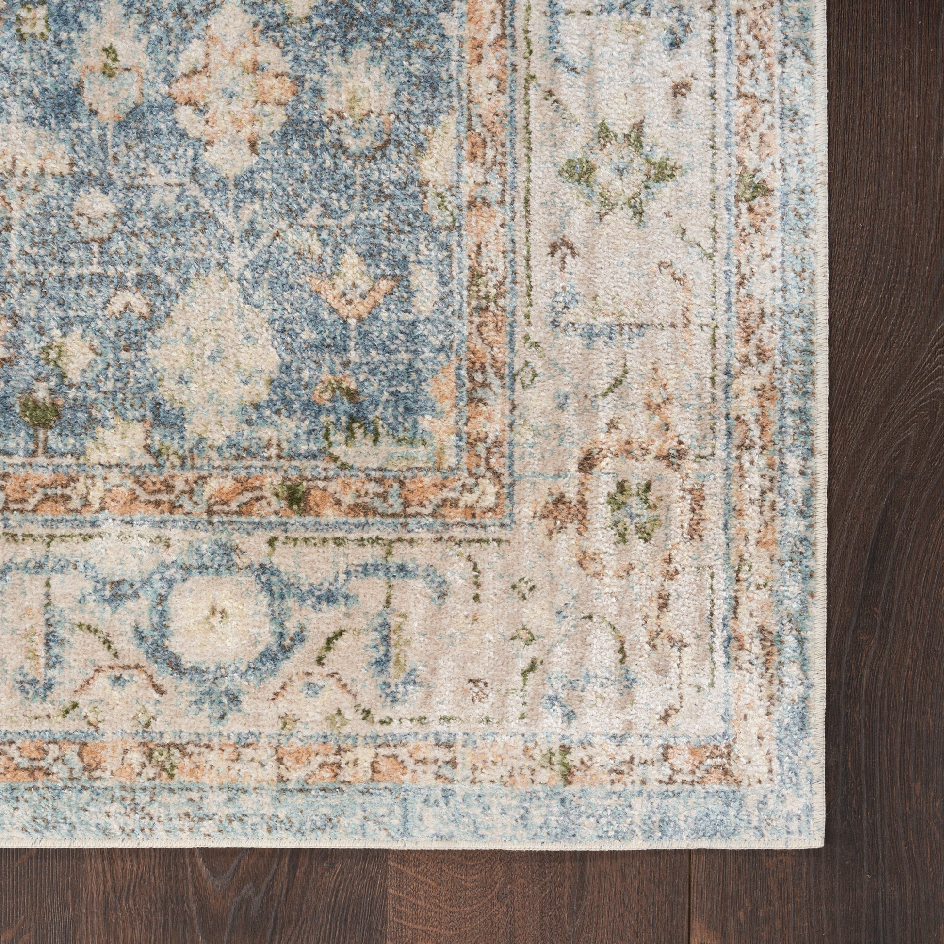 Blue and cream ornate area rug with peach border, distressed vintage style, on dark wood floor.