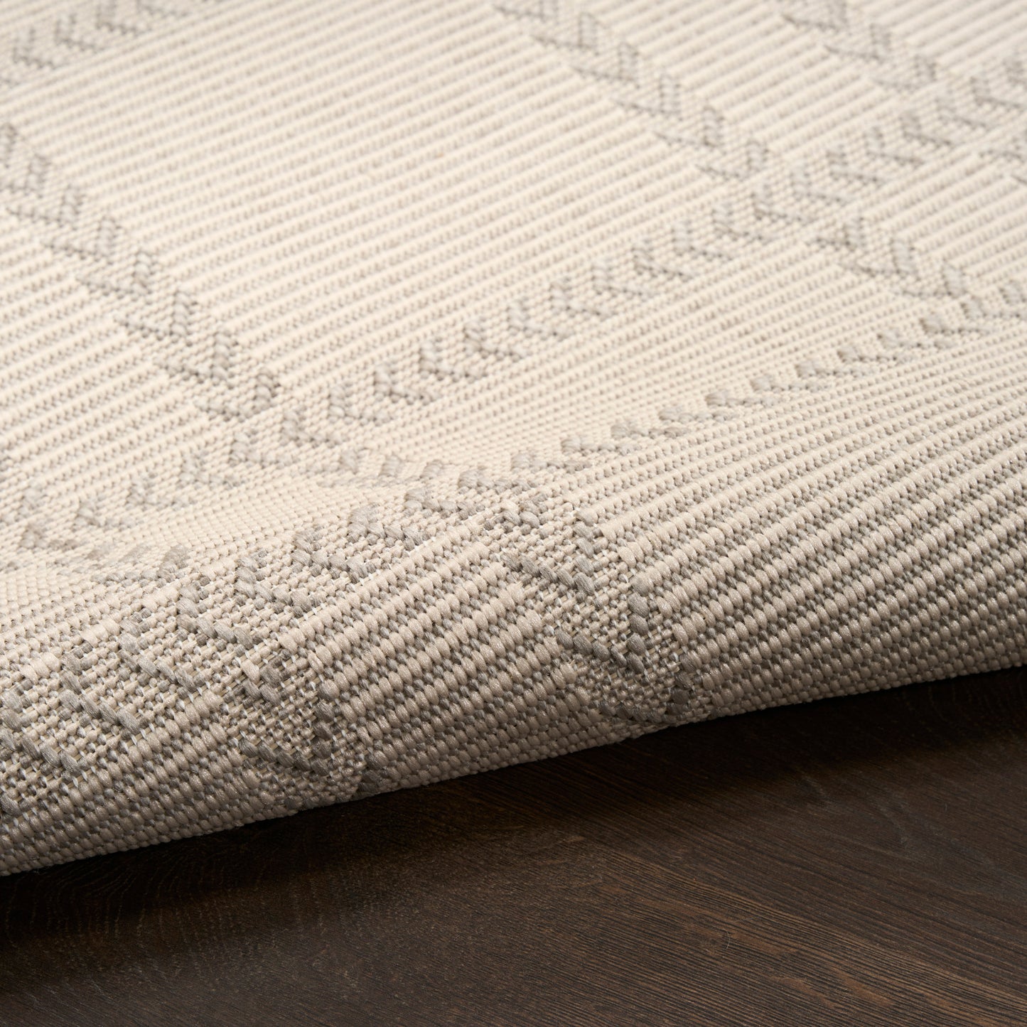 Beige woven rug with subtle diamond pattern and textured weave, folded edge on a dark wood floor.