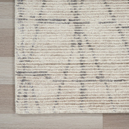 Fringed edge beige area rug with cream base and blue-gray linear pattern on light wood floor.