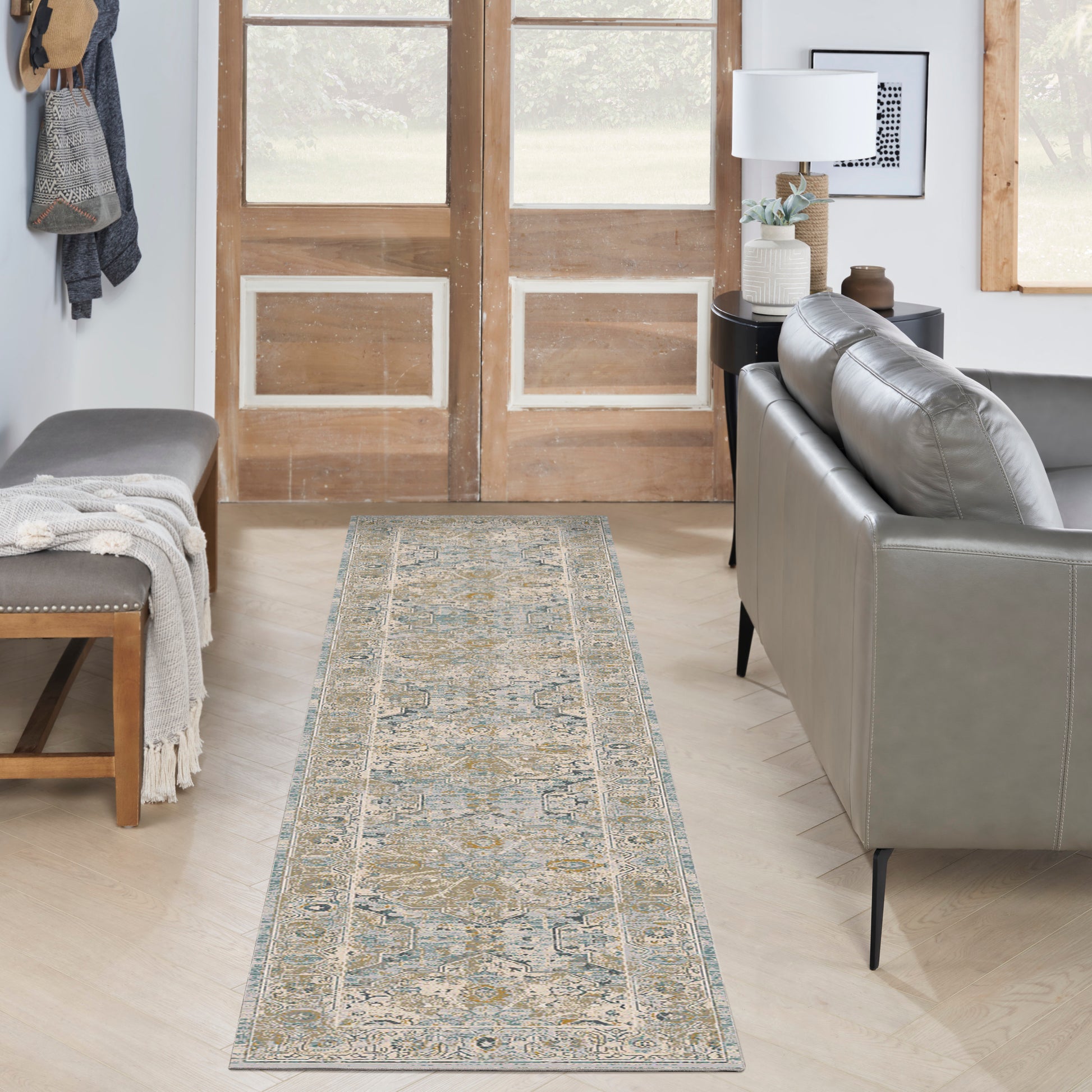 Living room entry with a long ornate blue-beige-gold runner rug, grey leather sofa, and wooden doors.