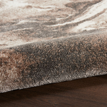 Close-up of a plush area rug with beige, brown & taupe tones, folded edge on dark wood floor.