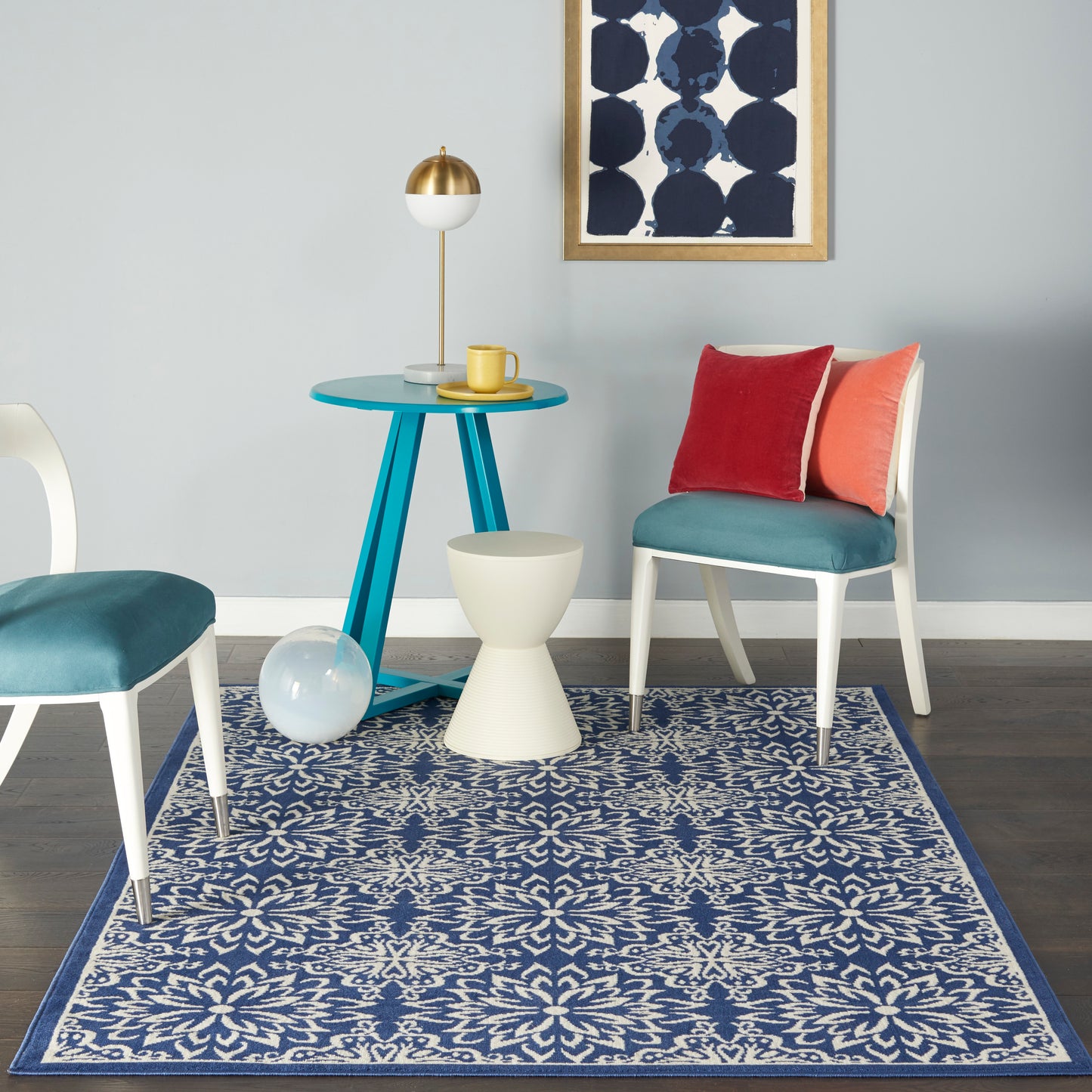 Mid-century living room with teal round table, white chairs on teal cushions, pedestal stool, blue patterned rug, navy art.