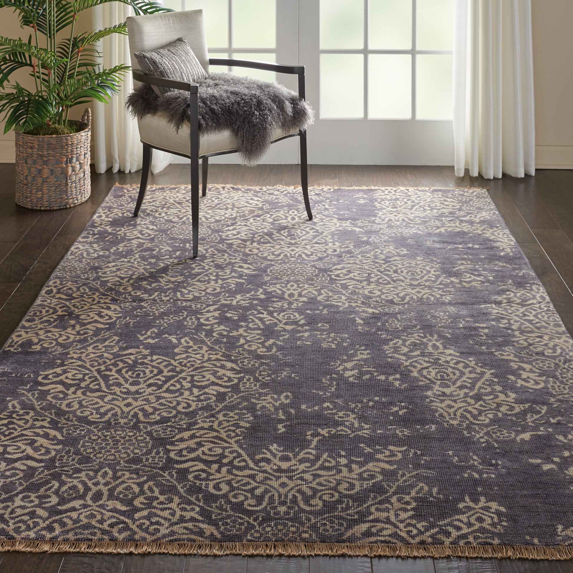 Gray-blue damask area rug with beige pattern and fringe under a chair with a gray faux-fur throw.