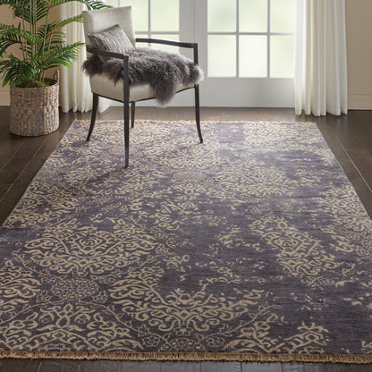 Gray-blue damask area rug with beige pattern and fringe under a chair with a gray faux-fur throw.
