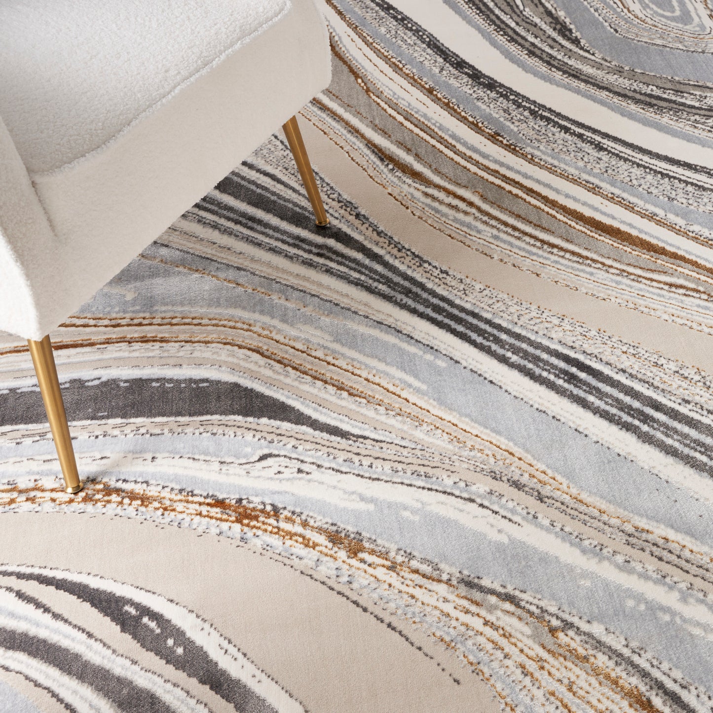 White boucle chair with gold legs resting on an abstract striped area rug in cream, gray, blue, and orange.