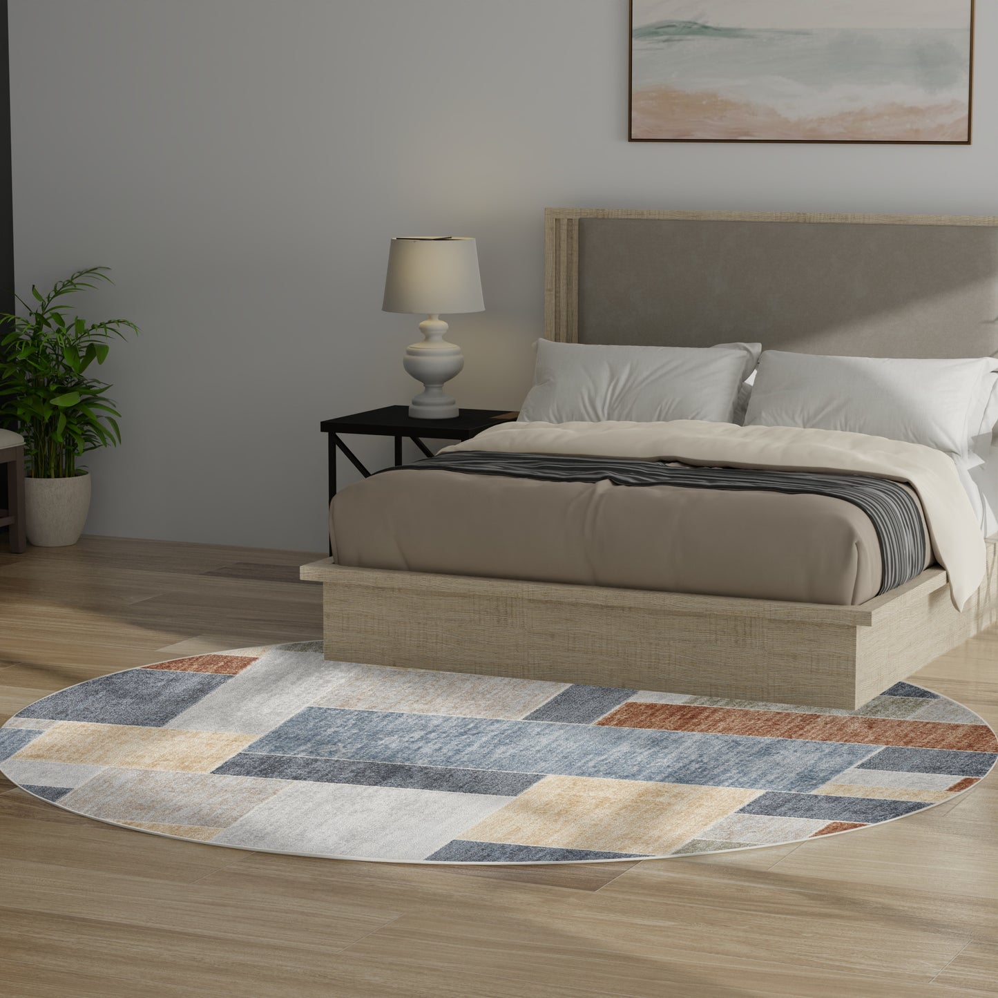 Round geometric rug in blue, tan and gray under a beige platform bed with a gray headboard; bedside lamp and plant nearby.