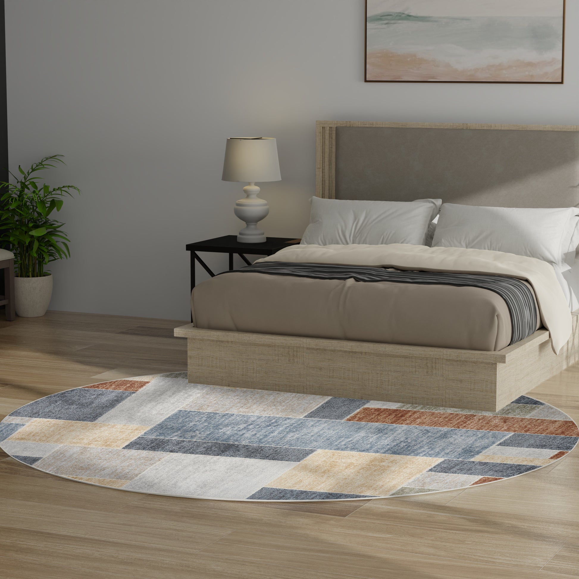Round geometric rug in blue, tan and gray under a beige platform bed with a gray headboard; bedside lamp and plant nearby.