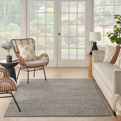 Bright living room with beige sofa, rattan chairs, gray rug, glass French doors to garden, greenery, and warm wooden accents.