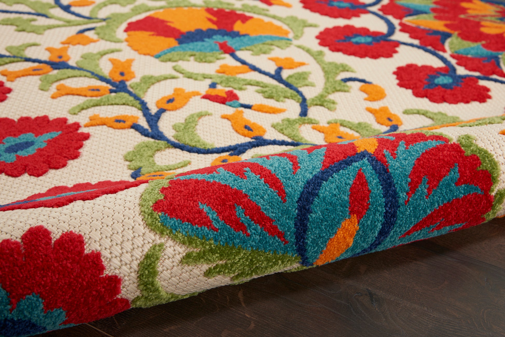 Close-up of a vibrant embroidered rug with red, blue and teal floral motifs on a beige background.