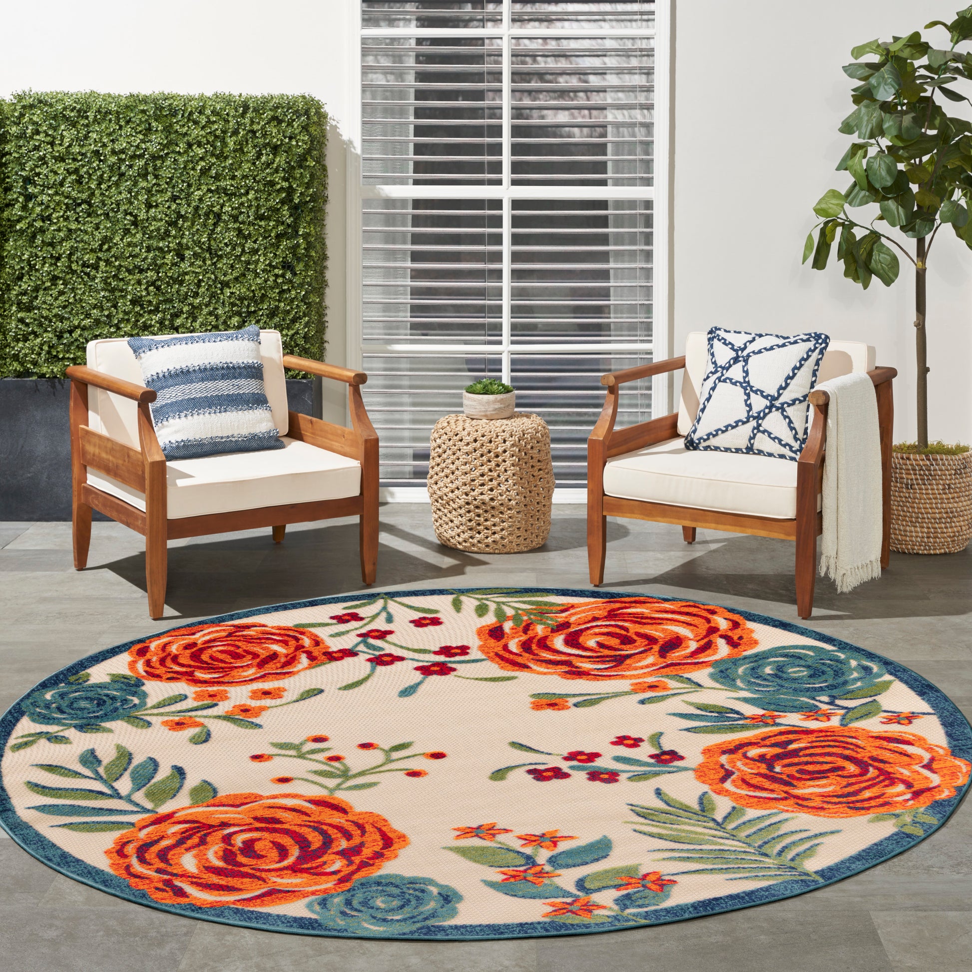 Round rug with orange roses and blue accents on a patio; two wooden armchairs with white cushions.