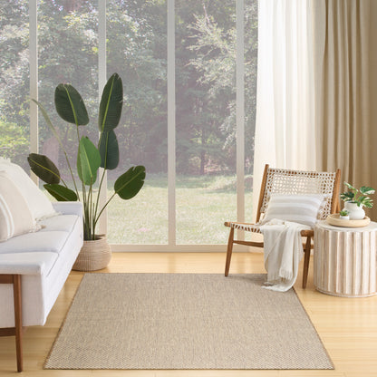 Bright living room with large windows, beige rug, white sofa, tall leafy plant, rattan chair, round side table, and curtains.