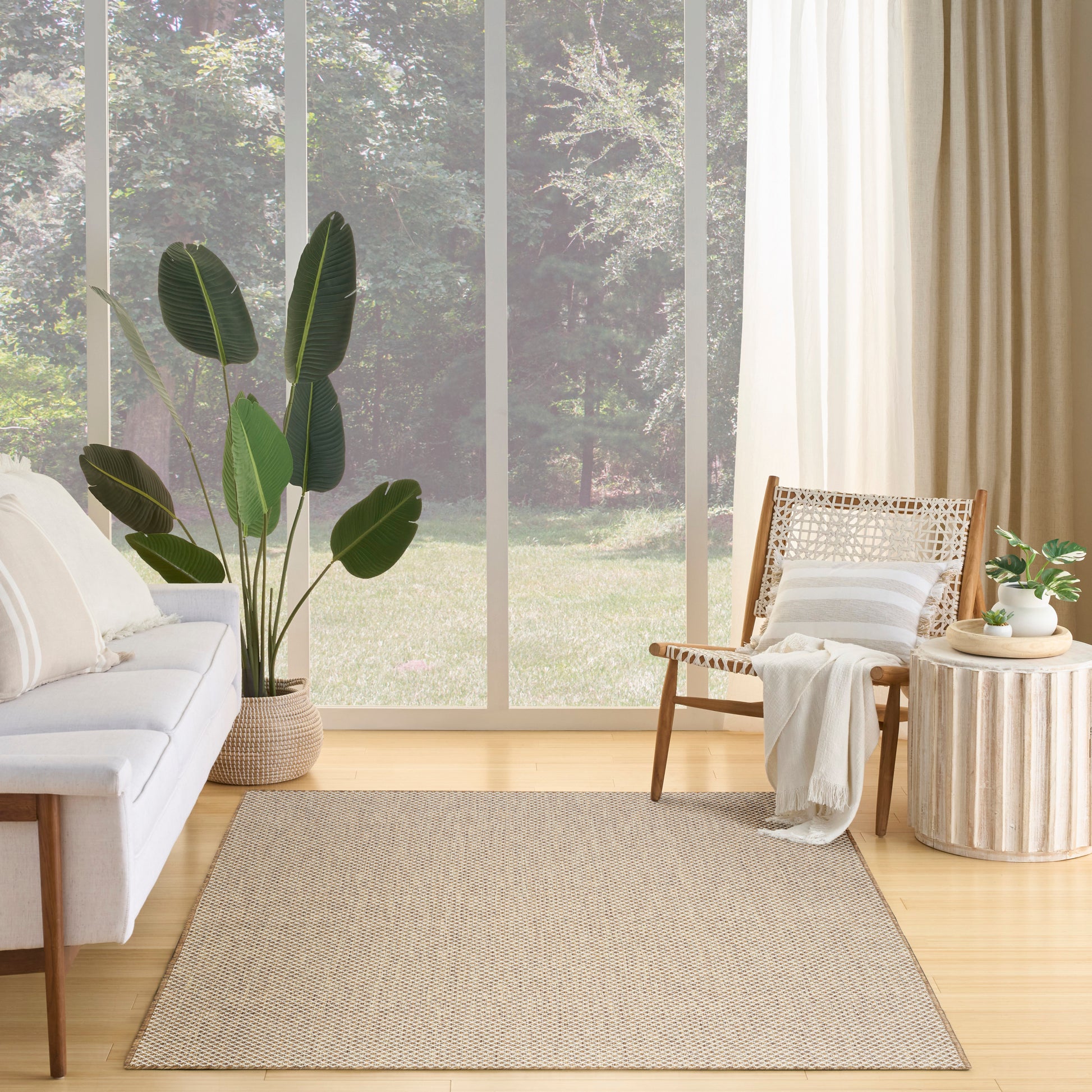 A bright living room featuring a 6' x 9' jute rug, cream sofa, cane-back chair, large-leaf plant and a round ribbed side table.