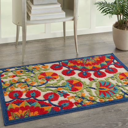 Bright multicolor floral area rug with blue border on gray wood floor beside a small shelf and plant.