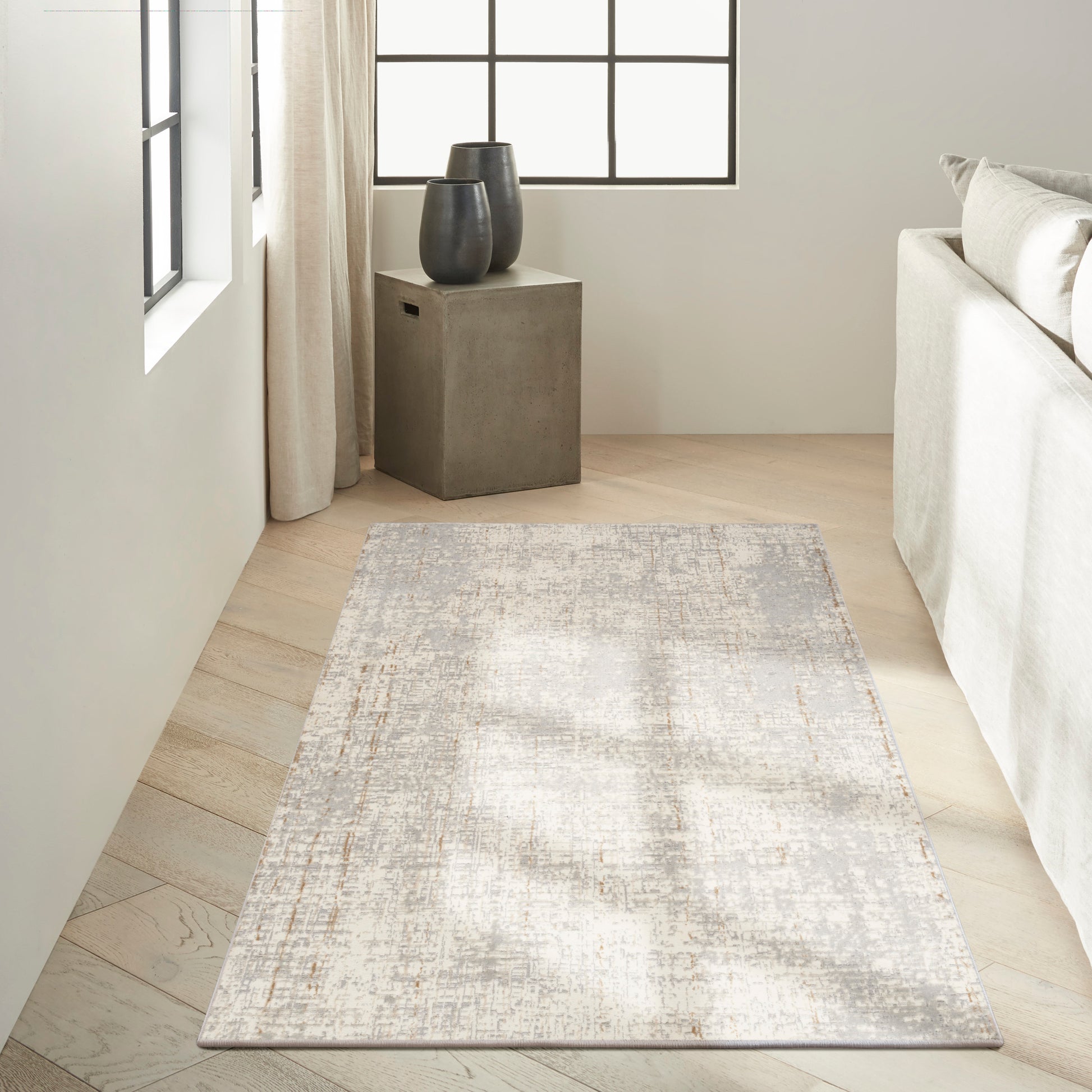 Neutral-toned abstract rug on light wood floor beside a concrete block side table with two dark ceramic vases.