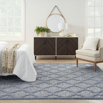 Modern bedroom with dark chevron dresser, round wood mirror, beige chair, blue patterned rug and white bedding.
