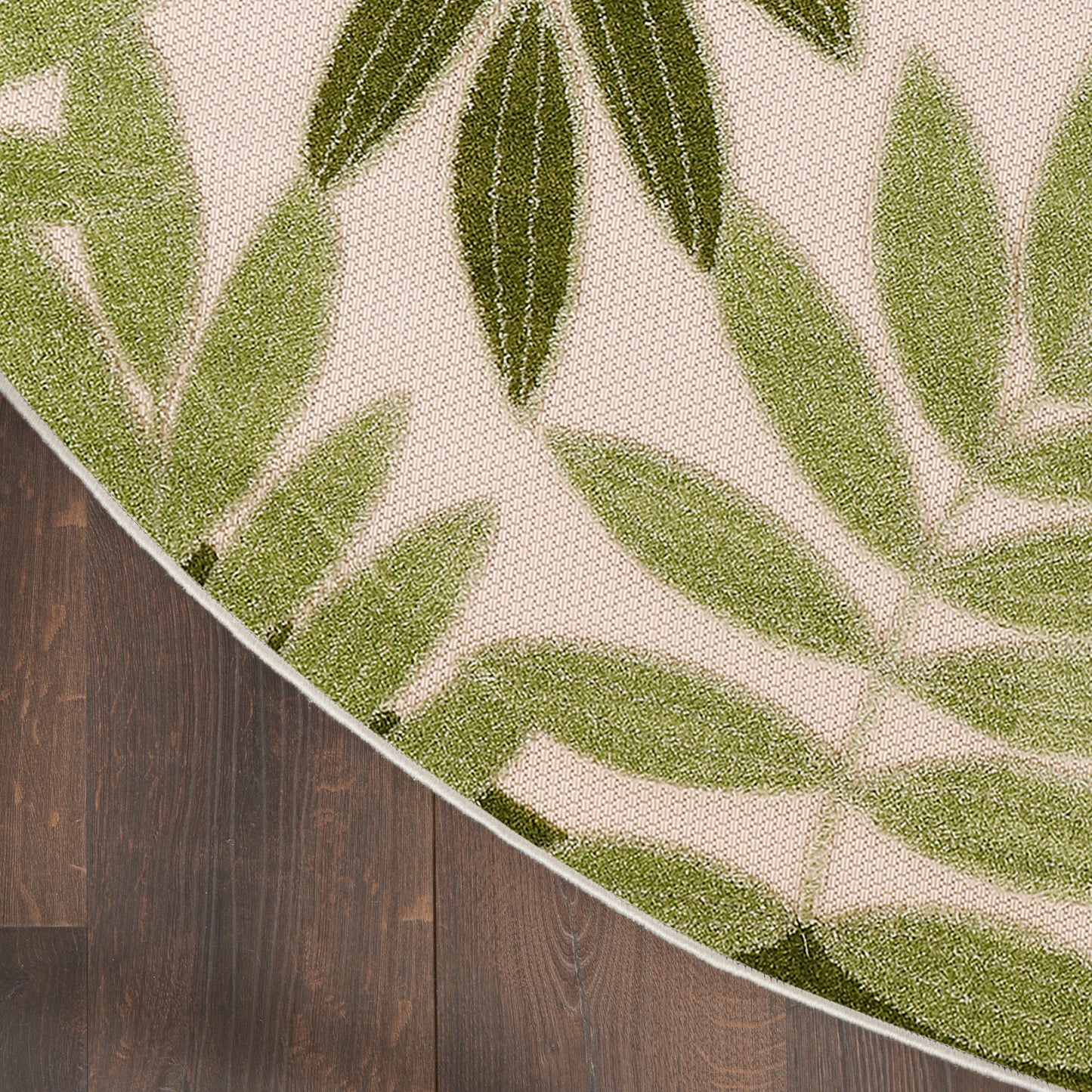 Round flat-woven rug with olive and light-green palm leaf pattern on beige, on dark wood floor.