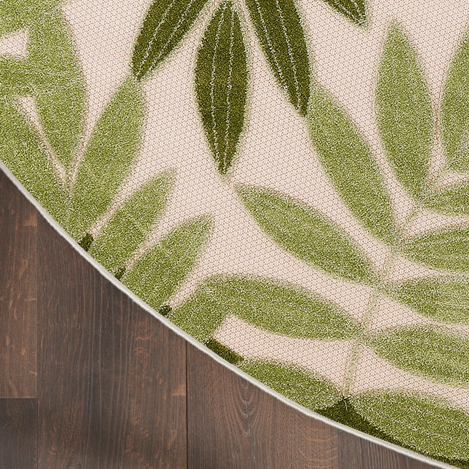 Round flat-woven rug with olive and light-green palm leaf pattern on beige, on dark wood floor.