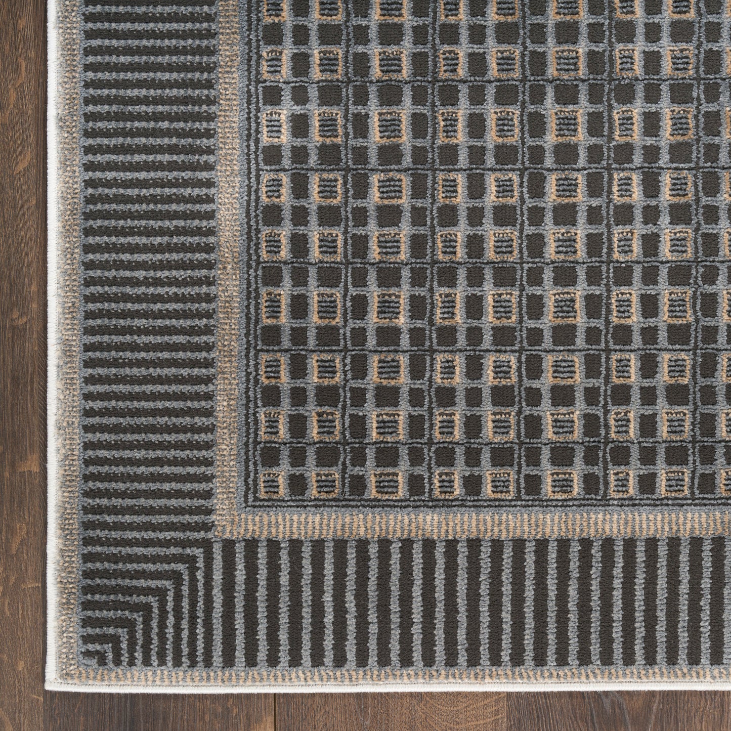 Dark gray geometric area rug with tan square accents and layered striped borders on a wooden floor.