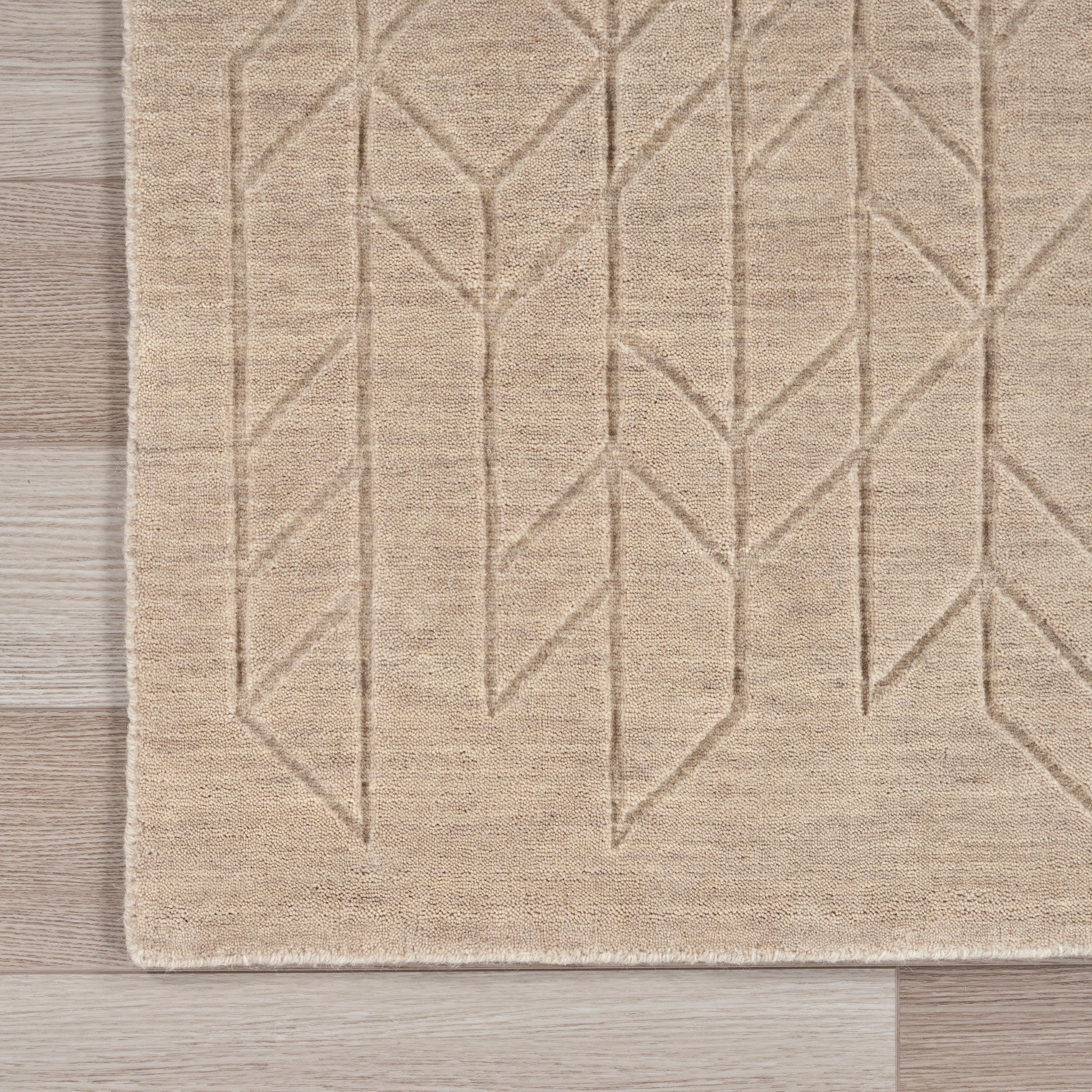 Beige woven rug with geometric chevron pattern and fringe edge on light wood floor, 2' x 3'.