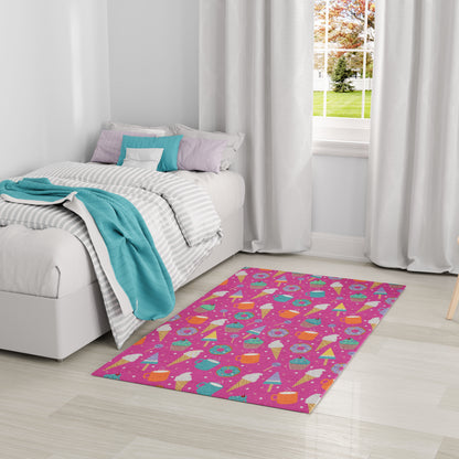 Bright pink kids' rug with multicolored geometric shapes on a light wood floor beside a white bed with teal throw.