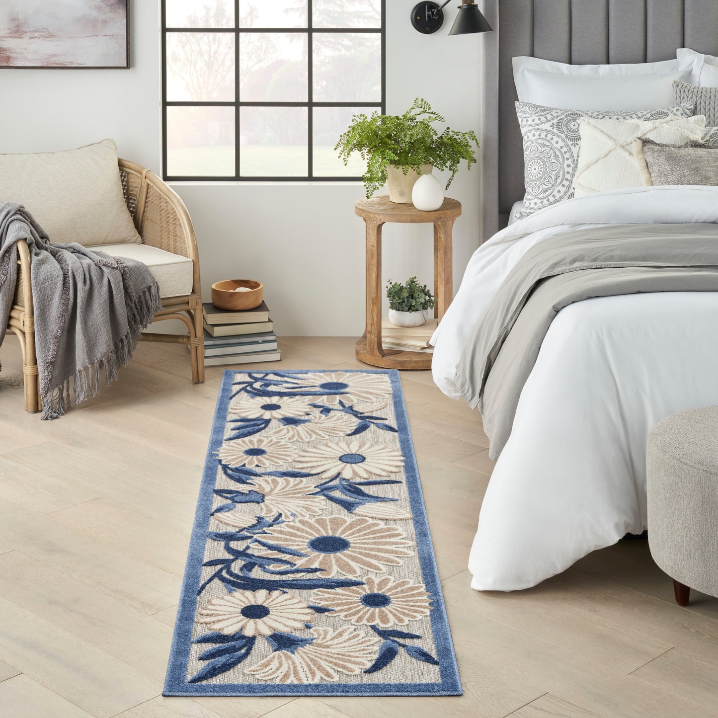 Narrow fabric runner rug with beige floral pattern and blue border on light wood floor beside a white bed.