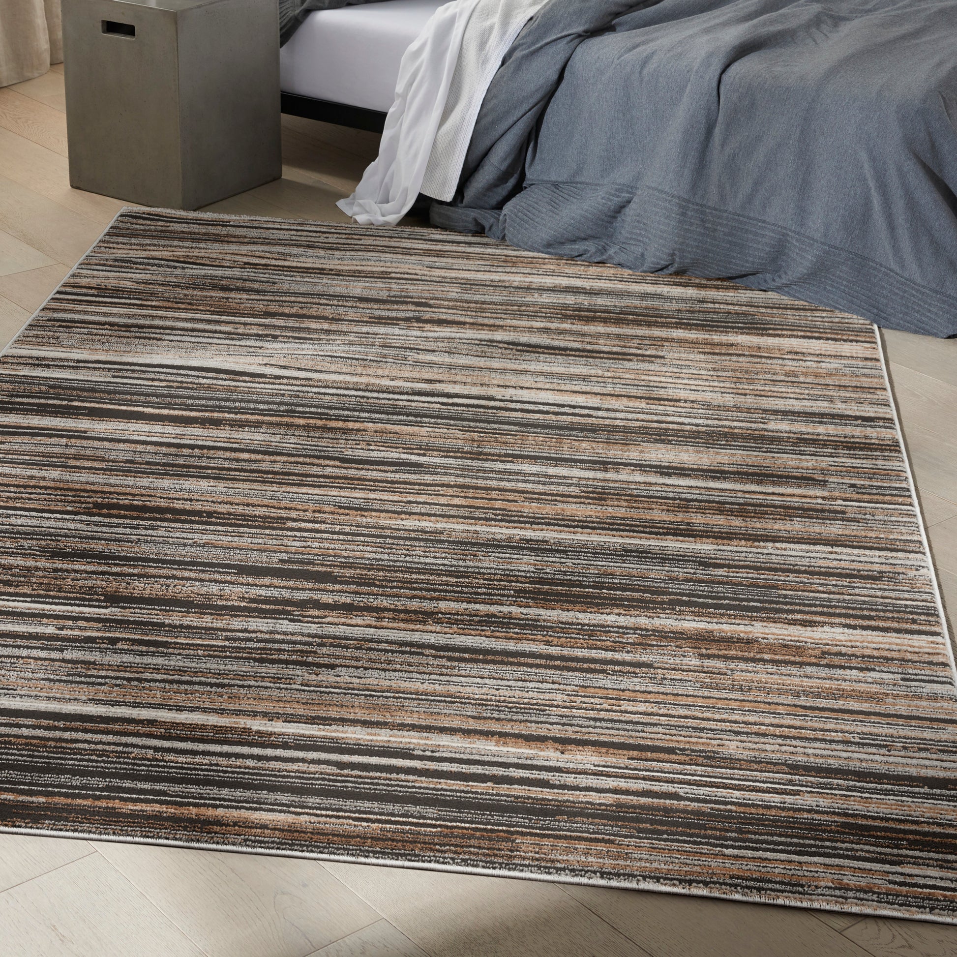 Rectangular striped area rug in brown, beige and cream tones under a bed with gray bedding.
