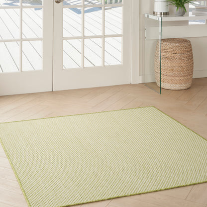 Rectangular light lime woven area rug on pale wood floor beside glass doors, with wicker basket and glass console.