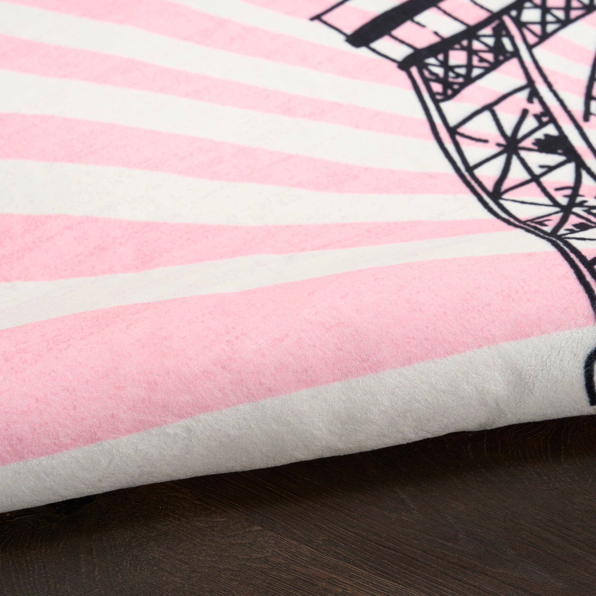 Soft plush rug in pink and white stripes with a partial black ferris wheel design; cozy rug on a dark wood surface.