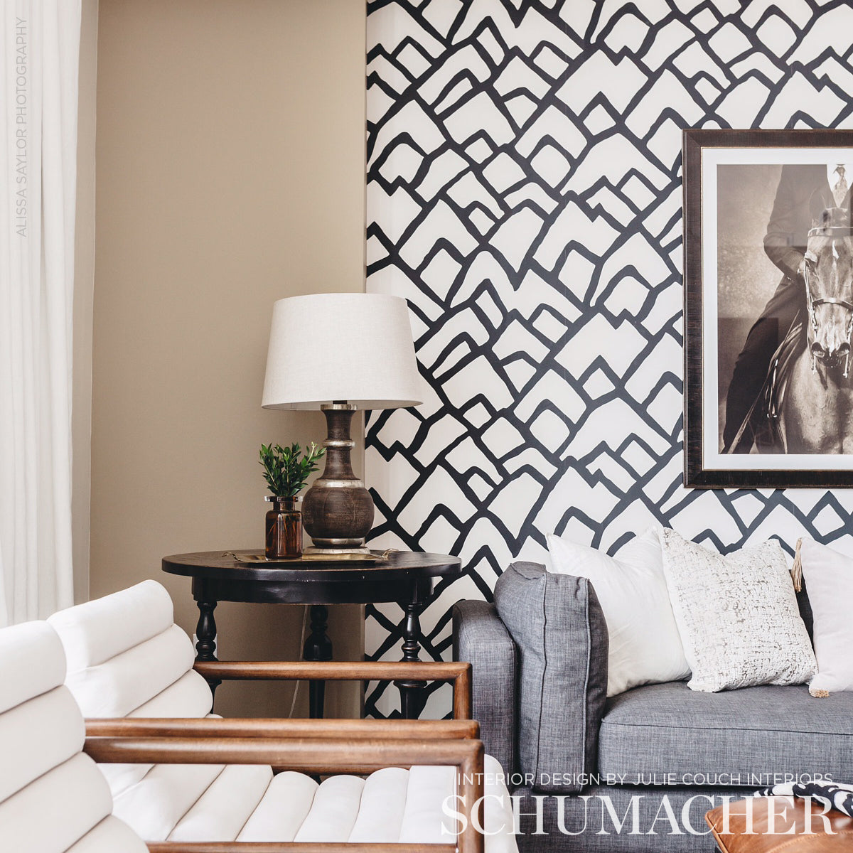 Bold black-and-white geometric wallpaper in a living room with beige wall, dark wood table, white lounge chairs and gray sofa.