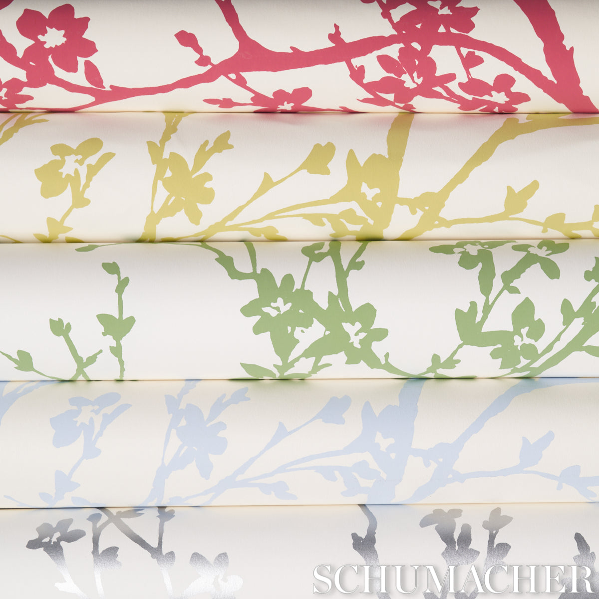 Folded white fabric bolts with red, yellow, green, and blue floral branch patterns; Schumacher watermark.