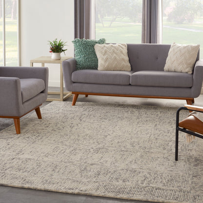 Grey mid-century sofa with matching armchair, two cream zigzag pillows and a green textured pillow, wooden legs, beige rug.