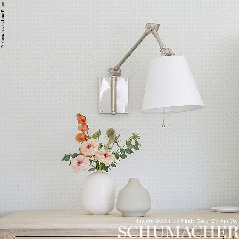 Wallpaper with a light diamond pattern on the wall behind a light wood table with white vases and pink flowers.