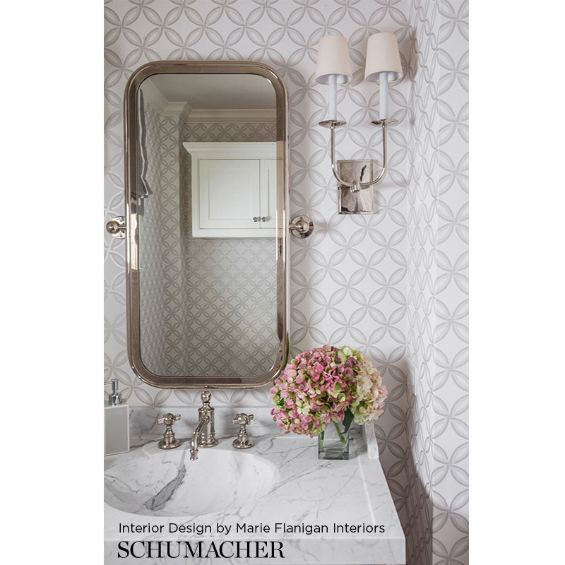 Oval metallic-framed mirror above a marble vanity, two wall sconces, geometric wallpaper, and a pink bouquet.